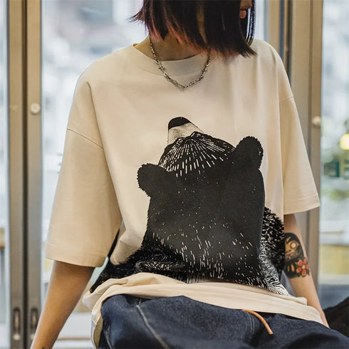 Person wearing a beige t-shirt with a black bear graphic design.